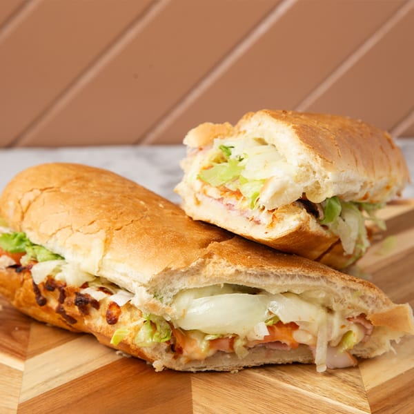 Two halves of a toasted sub sandwich with melted cheese, lettuce, and meat on a wooden board.