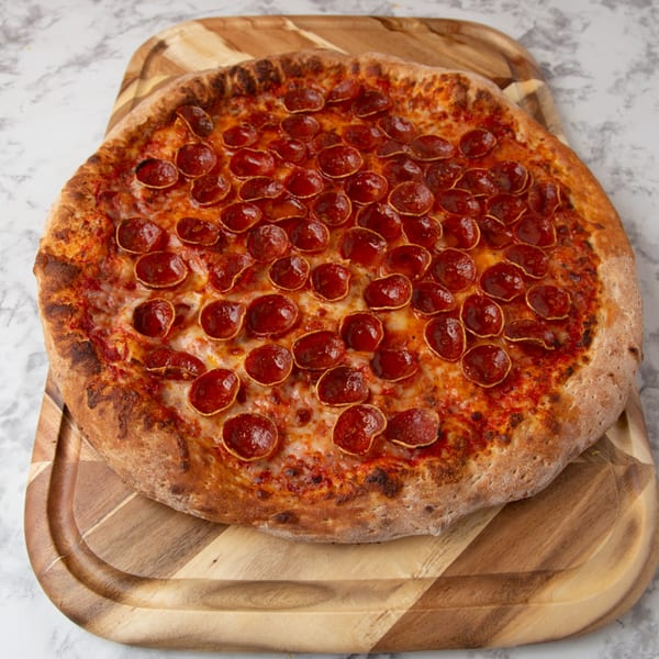 A large, round pepperoni pizza from Tomatoes II Pizzeria on a wooden cutting board.
